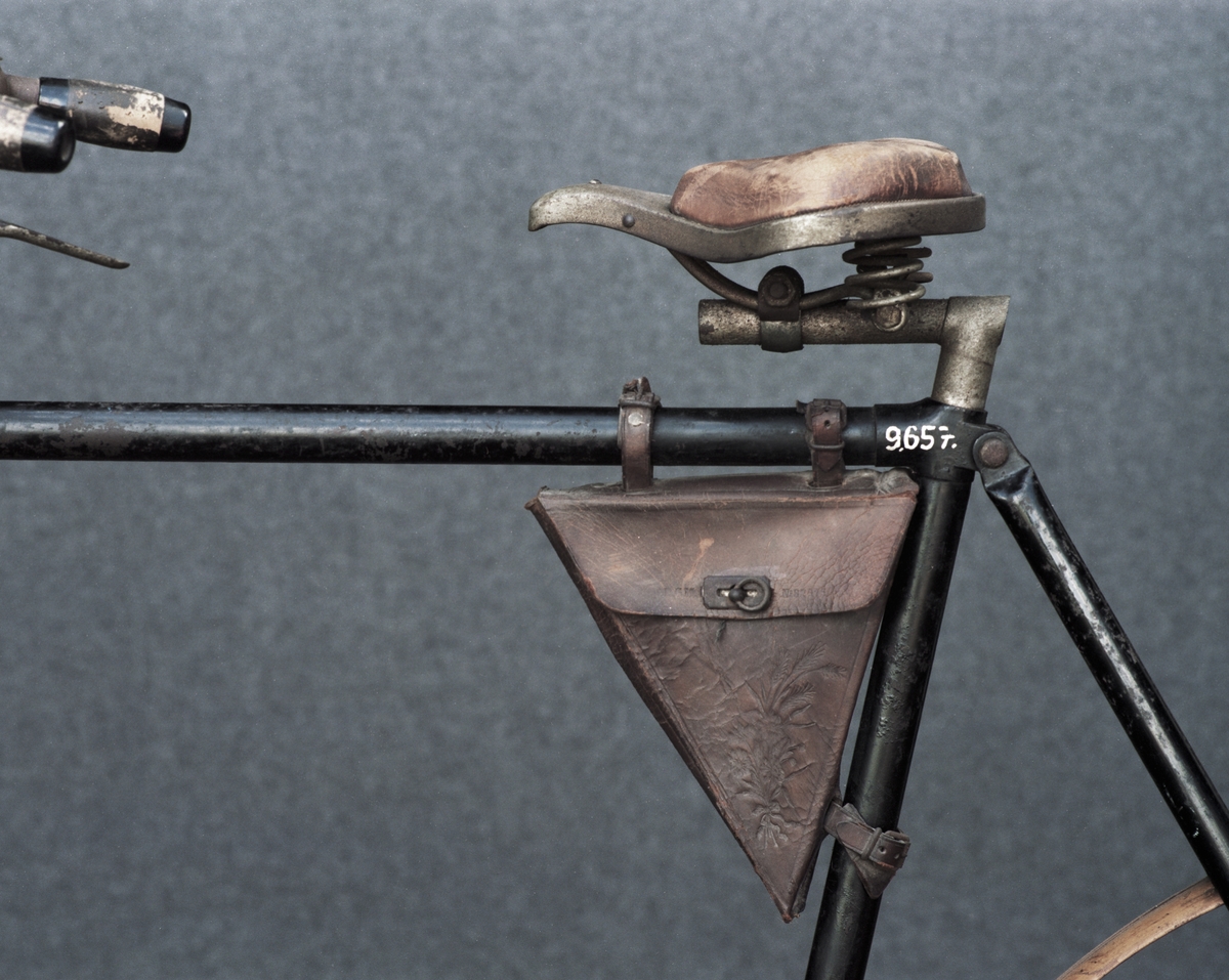 Tvåhjulig cykel med vertikaltrampning, herrmodell. Cykeln är utrustad med två sabelfästen. Träfälgar och träskärmar. Amerikansk ringklocka.
Tillbehör: Verktygsväska.