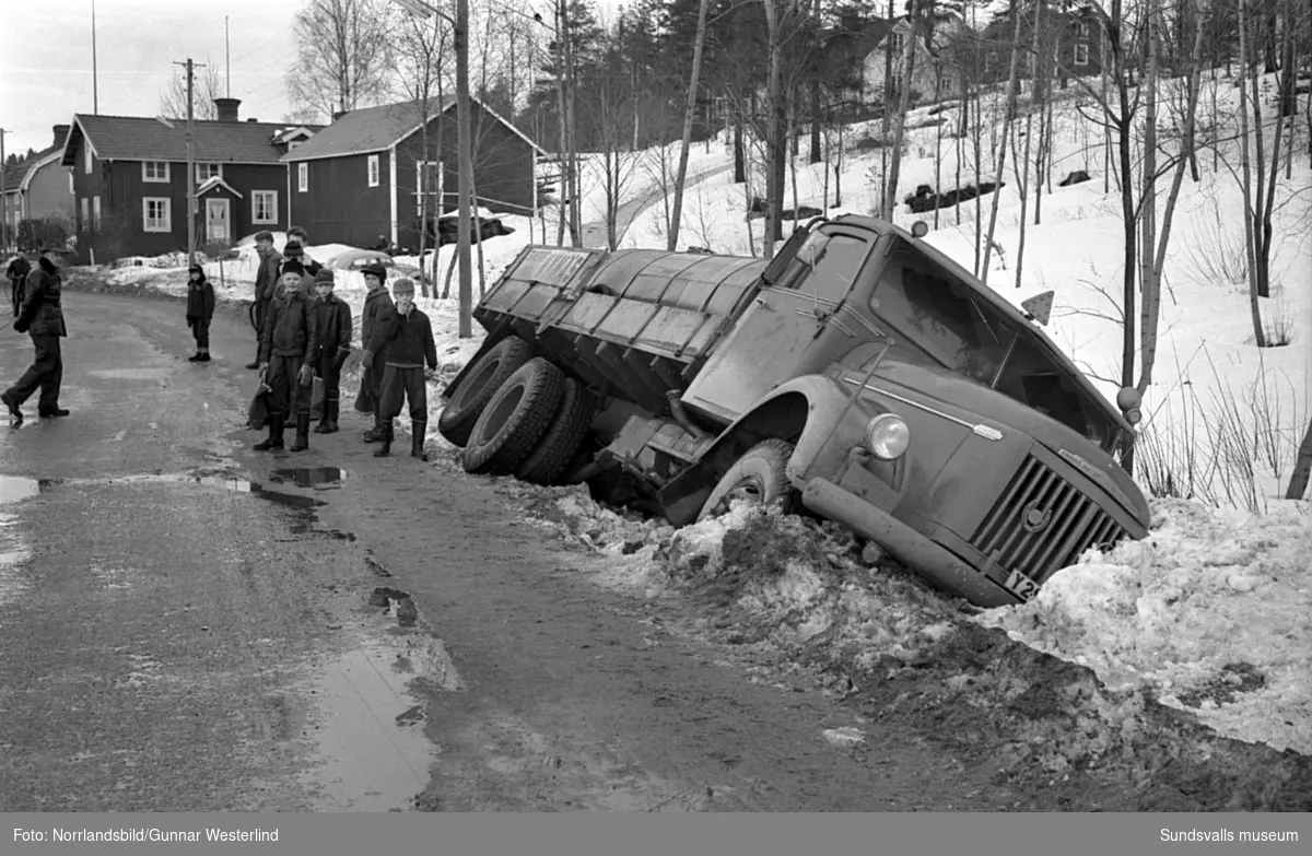 En tankbil har kört i diket i Essvik, ungefär där nuvarande korsningen mellan gamla Essviksvägen och Mistelvägen ligger. En del av byggnaderna som syns bakom finns fortfarande kvar (2016).