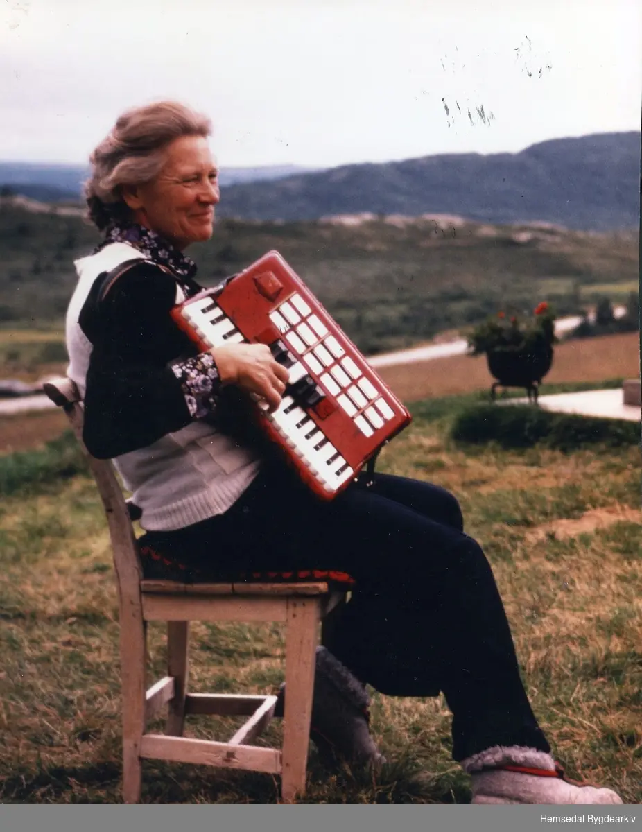 Birgit (Billa) Jordheim, fødd Torset 1925, har teke med trekkspelet ut på vollen.