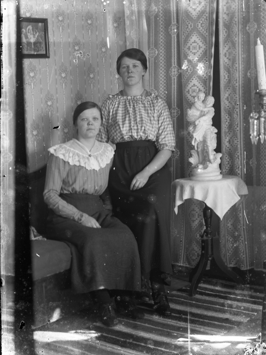 Gruppbild av två kvinnor fotograferade inomhus. Fotografens systrar Signe Sikén, sittande och  Anna Sikén stående.