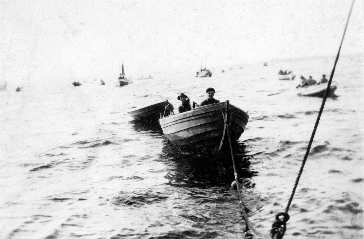 To fiskere i en robåt som taues av annet fartøy.