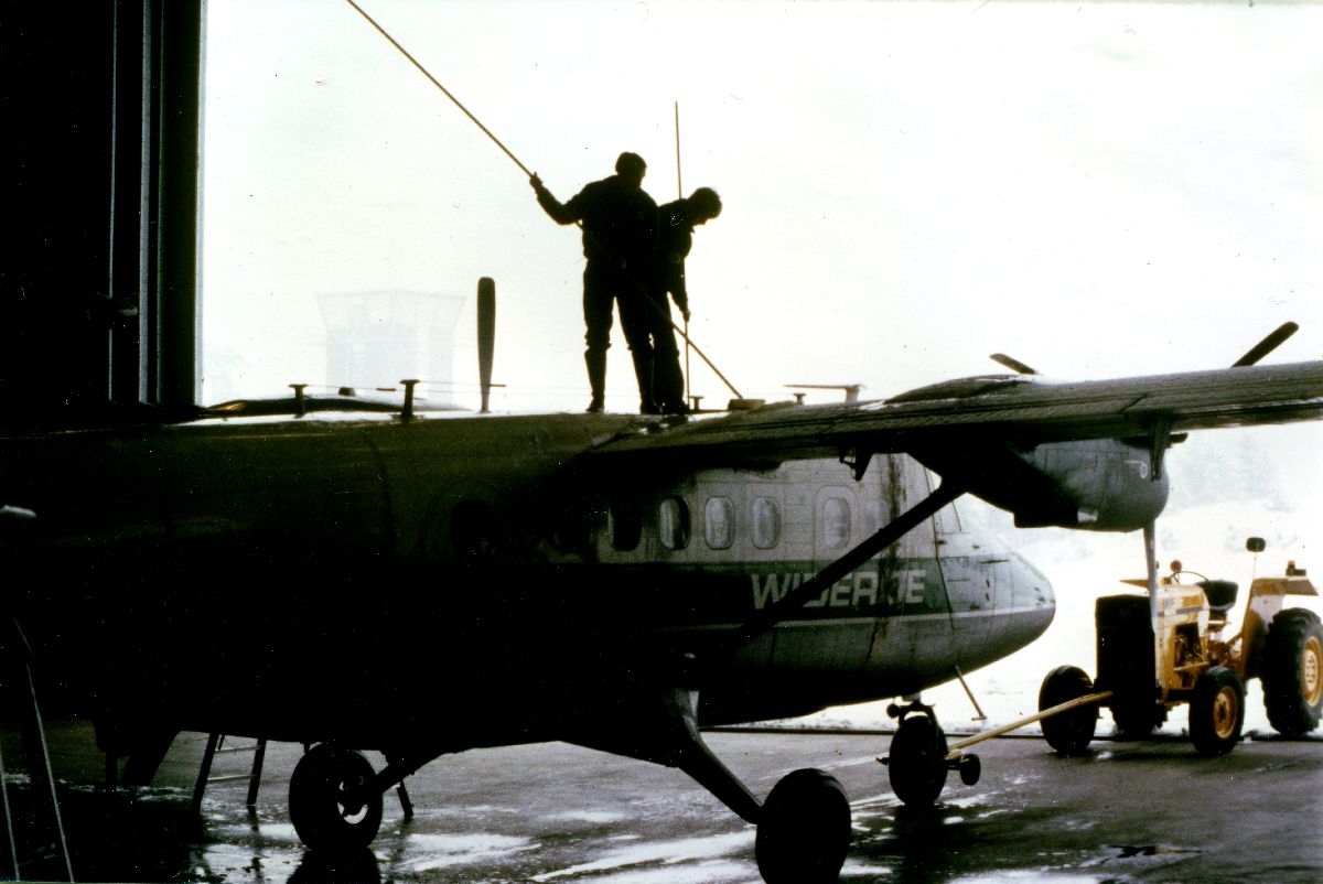 Landskap. Hangar. Et fly, DHC-6 Twin Otter fra Widerøe blir vasket av to personer, flyteknikere.