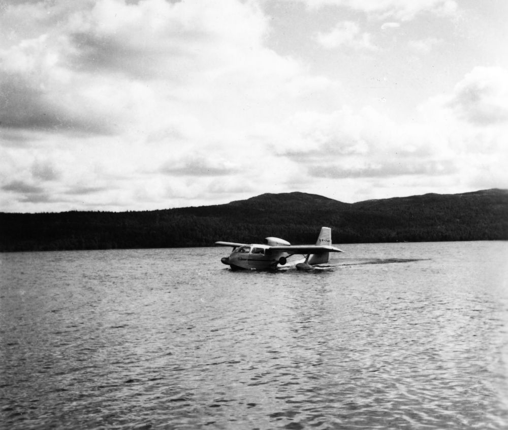 Landskap. Sjø. Et fly, LN-PAF, Republic Seabee fra Widerøes Flyveselskap & Polarfly AS, kommer taxende på  sjøen. I bakgrunn skogkledde åser.