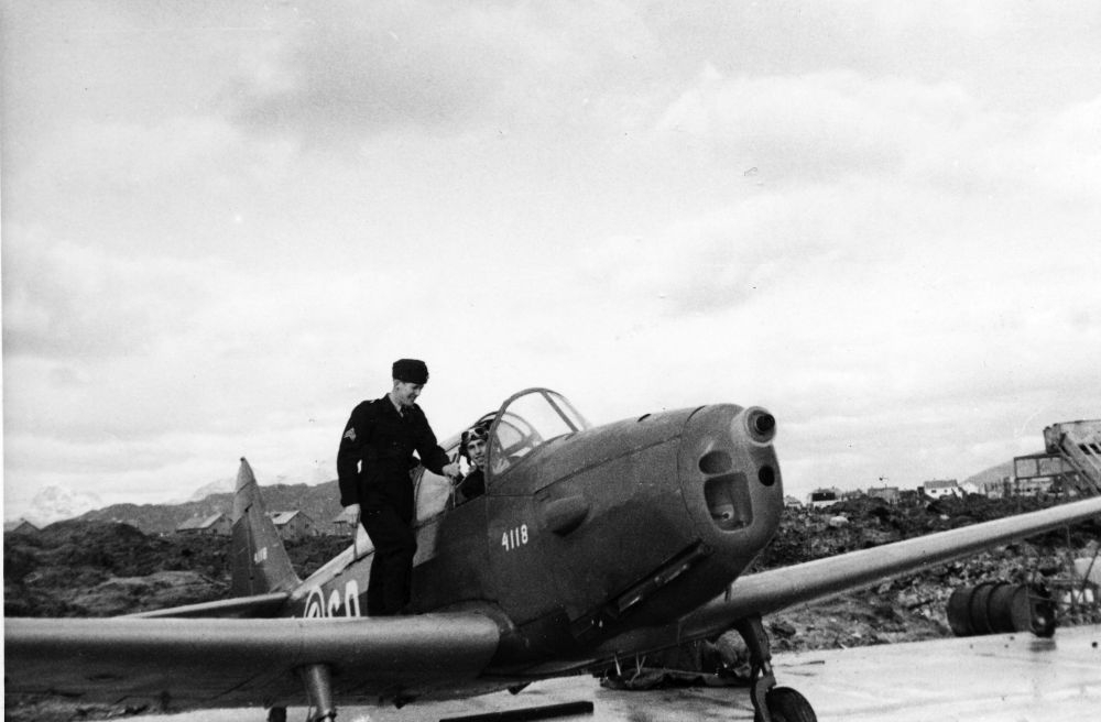 Lufthavn/Flyplass. Bodø. Et militært skolefly av typen Fairshield Cornell.  To personer, en sitter i cockpit og den andre står på vingen.