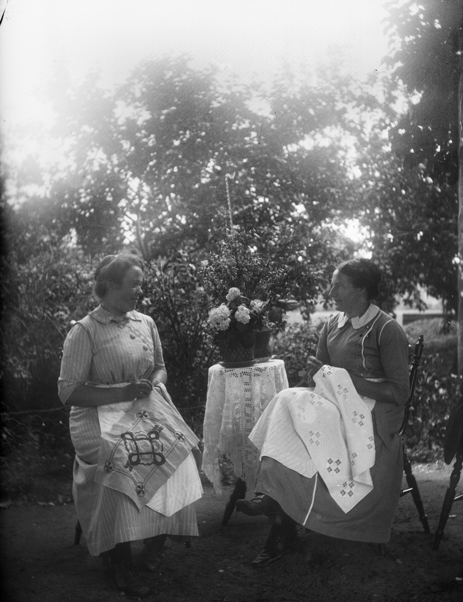Två kvinnor broderar i trädgården, 1910-talet