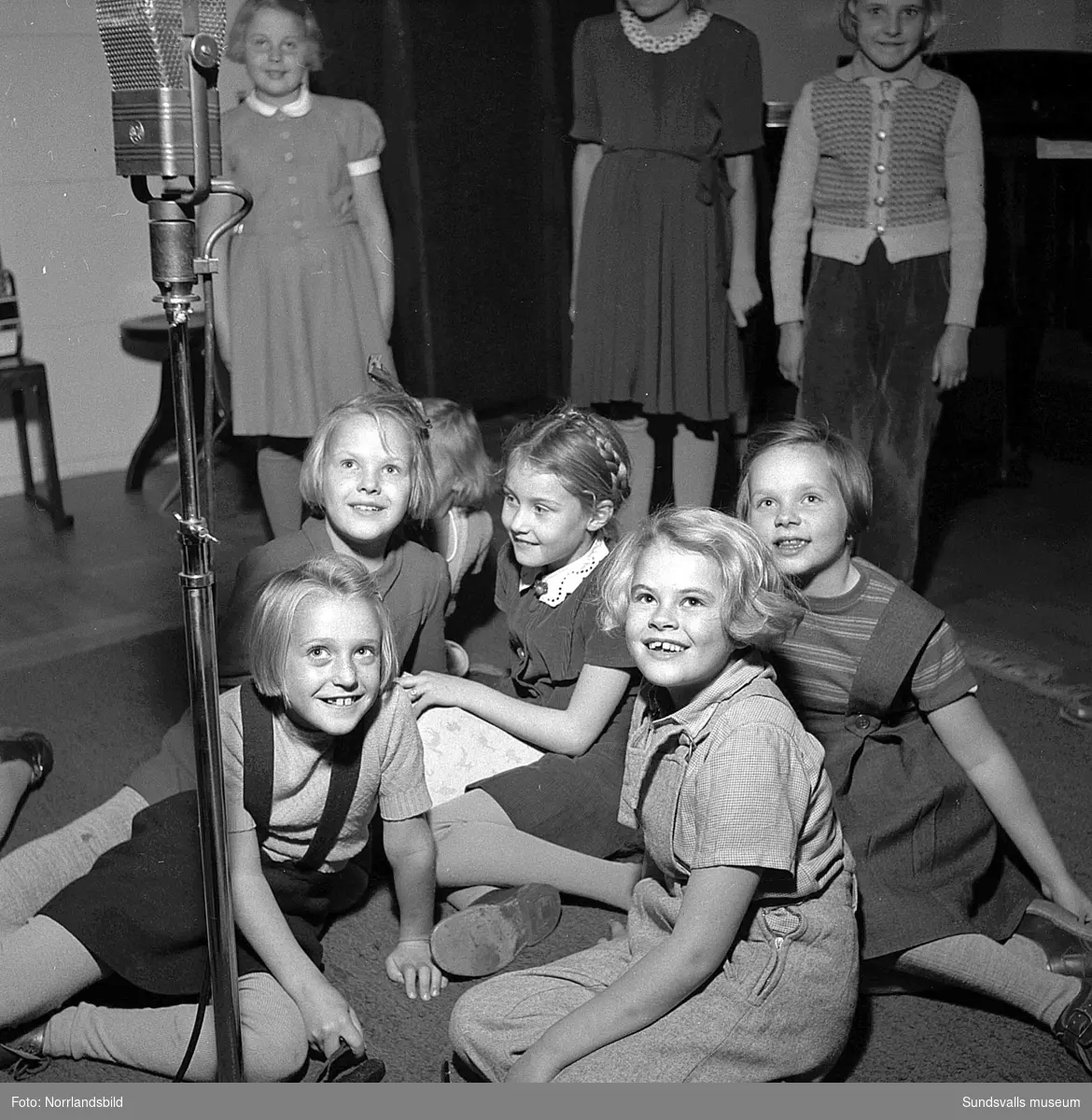 Barnradioprogrammet Önskevisan spelas in i Sundsvall. 30 småttingar hade kommit för att provsjunga varav tio valdes ut att medverka i det tjugo minuter långa direktsända programmet som sändes en gång i månaden. På bild fyra är det sjuåriga Berit Lundberg som sitter i knät på programledarinnan fru Birgitta Bohman, Radiotjänst.