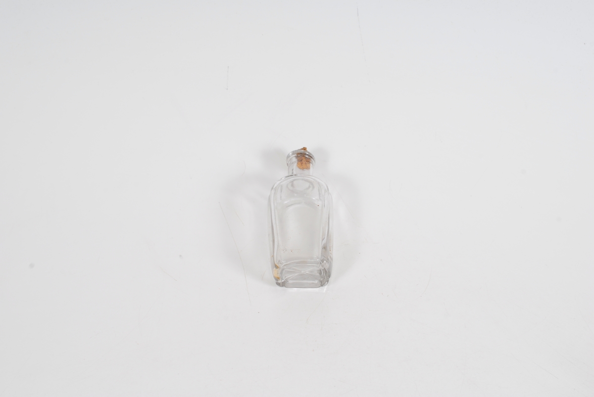 Gglasset er bueformet ved flaskens hjørner/kanter og i bunnen er det et enkelt blomsterlignende motiv. 