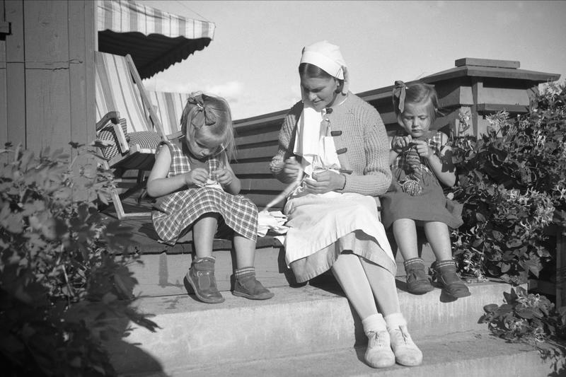 En kvinne og to barn sitter på en tapp og strikker. (Foto/Photo)
