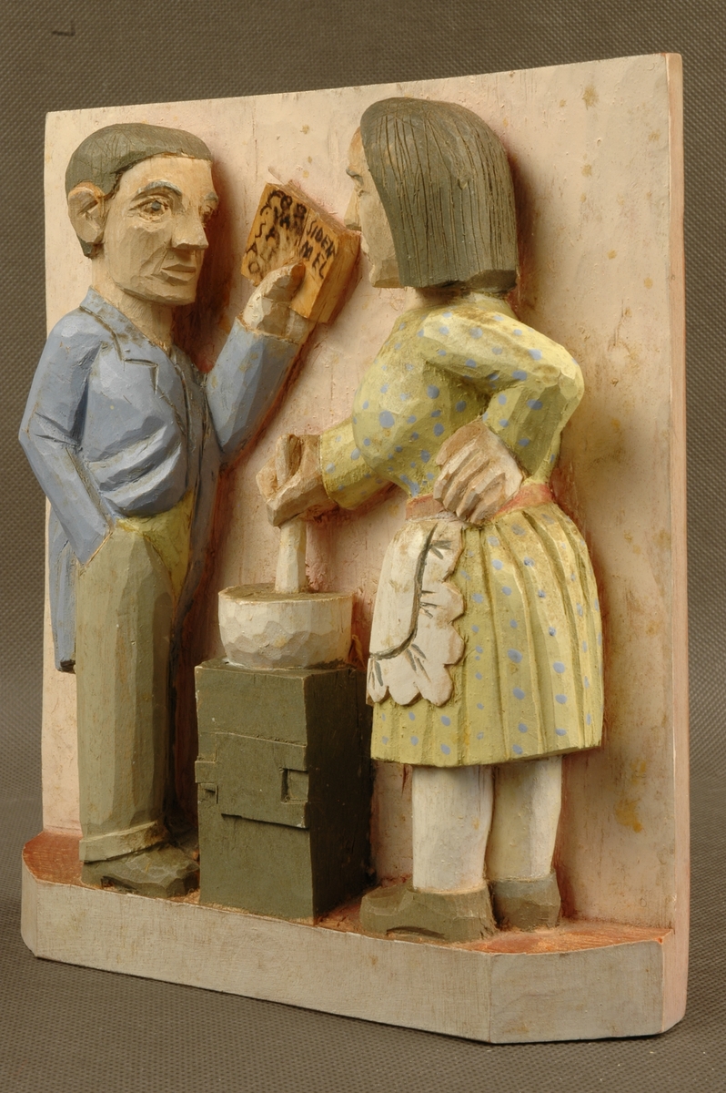 Kvinne- og mannsfigur. Mannen holder en bok, kvinnen rører i en gryte.