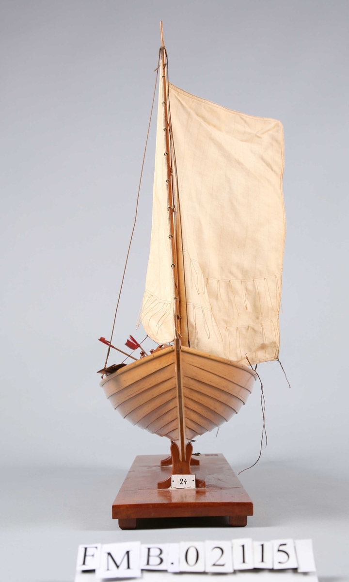 Modellbåt med mast og to seil. Den har 3 årer, 2 bøyer, et garn og en dregg.