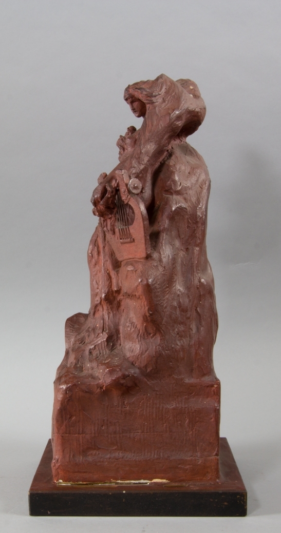 Kvinna, Sappho, stående håller en trälyra med metallsträngar i ena handen. I andra handen, tryckt mot bröstet, blommor. Lutad mot klippformation.