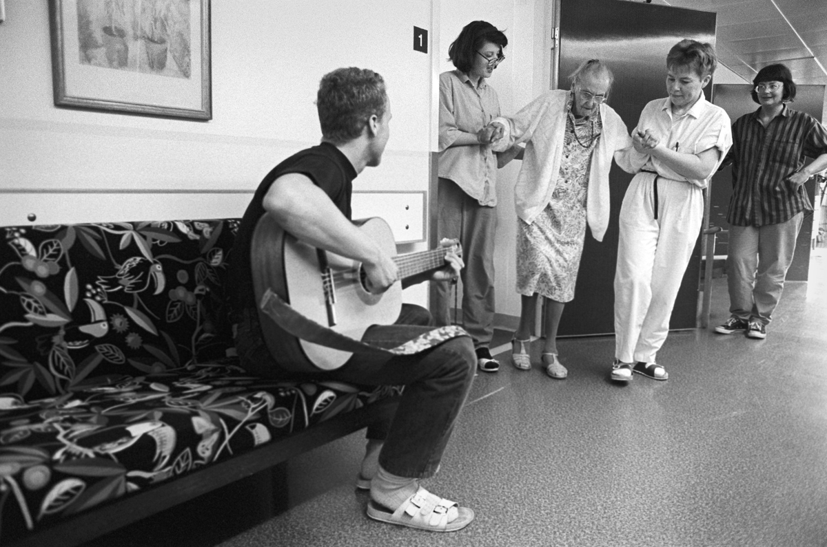 Eva Eriksson och Monika Näslund hjälper Vally Wanström fram till Ole Olsen som undehåller på gitarr, Tunåsens sjukhem, Uppsala 1992