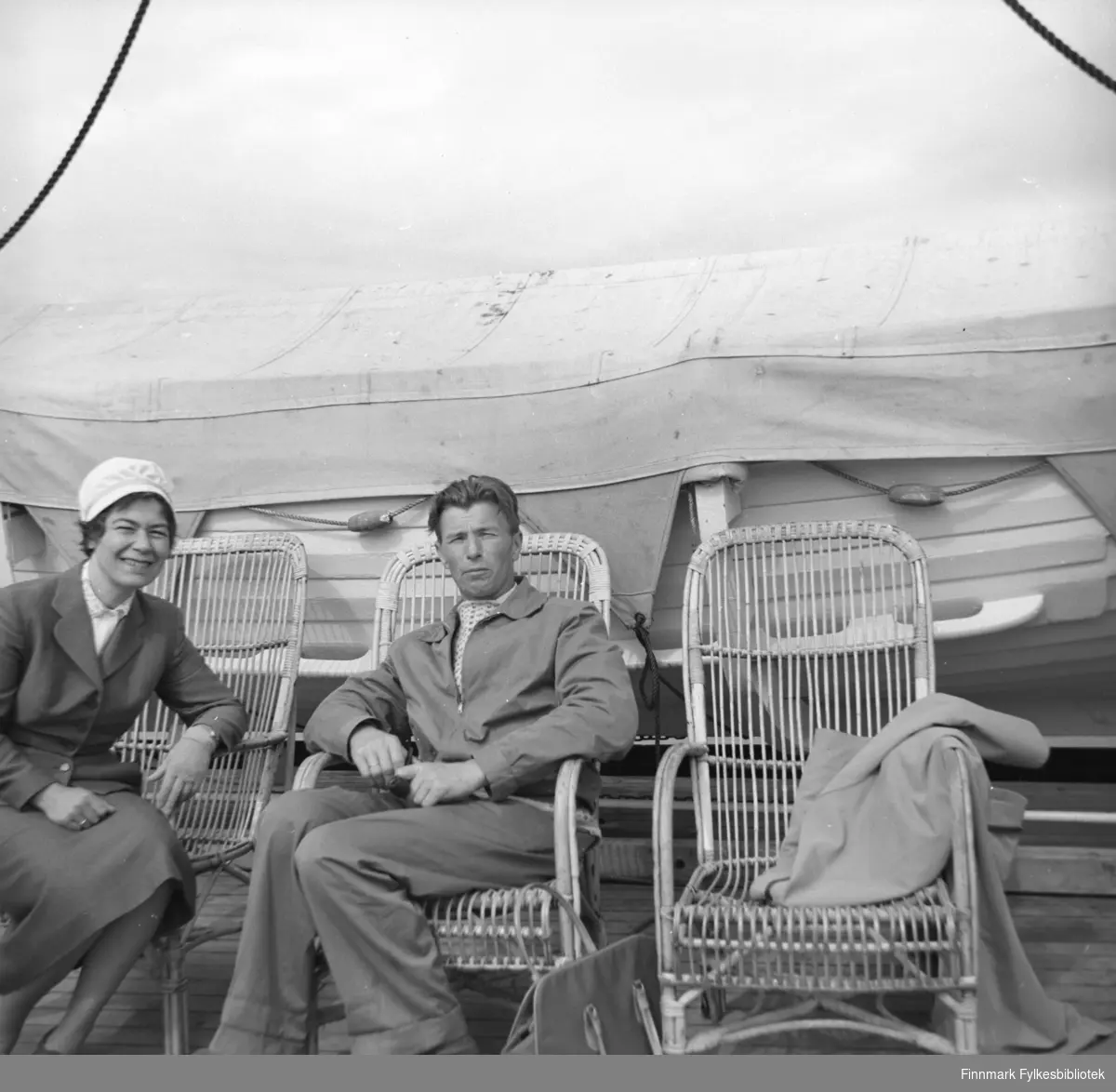 Jenny og Eino fotografert sittende i dekkstoler rett foran en livbåt.