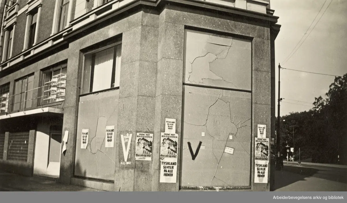 Ole M. Engelsens fotografier fra okkupasjonsårene i Oslo..Bygård på hjørnet av Drammensveien og Kronprinsens gate. Plakater med "Tyskland seirer på alle fronter" og "Front mot bolsjevismen - Hvor står du i dag?".Foto 27 juli 1941.