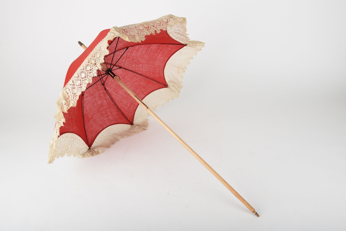 Liten parasoll med trehåndtak, kledd med rød tekstil med hvit blondekant.