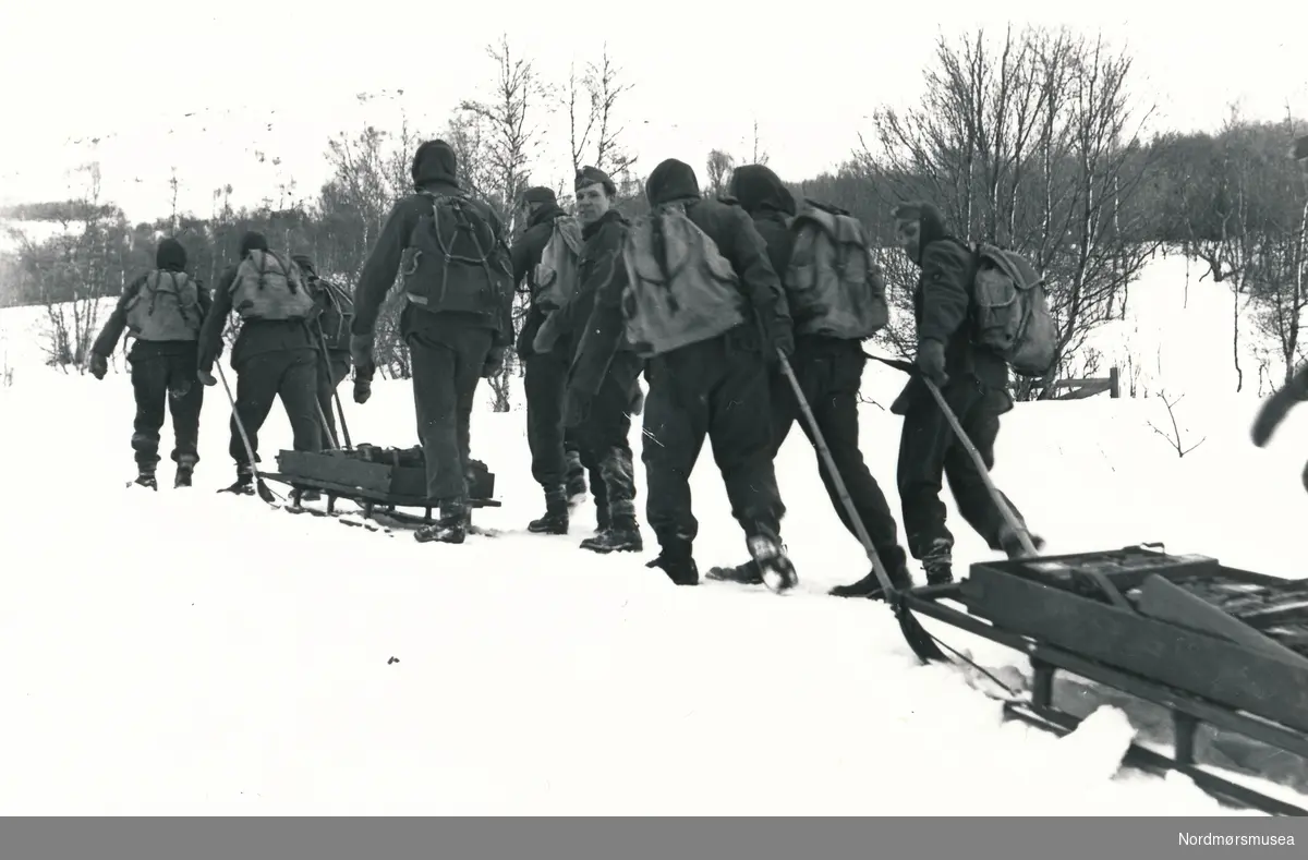 Soldater som går på ski. To av dem har med seg pulk.