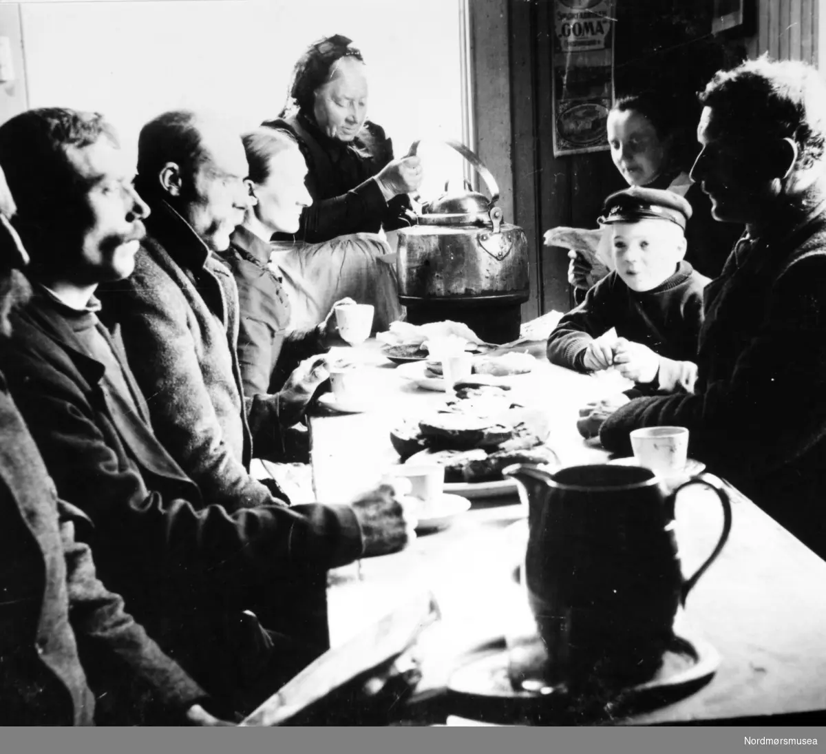 Et interiørfoto fra Marit Fladvads kafe, hvor vi ser en gruppe personer sittende rundt et matbord, mens Marit Flatvad tar imot bestillingen.Kafeen lå ved Fisketorget. Bildet er datert til 1890. Se også foto fra Gamle Kvernes Bygdemuseums fotosamling, med reg. nr.
GKB-25702.
Fra Nordmøre Museums fotosamlinger.
