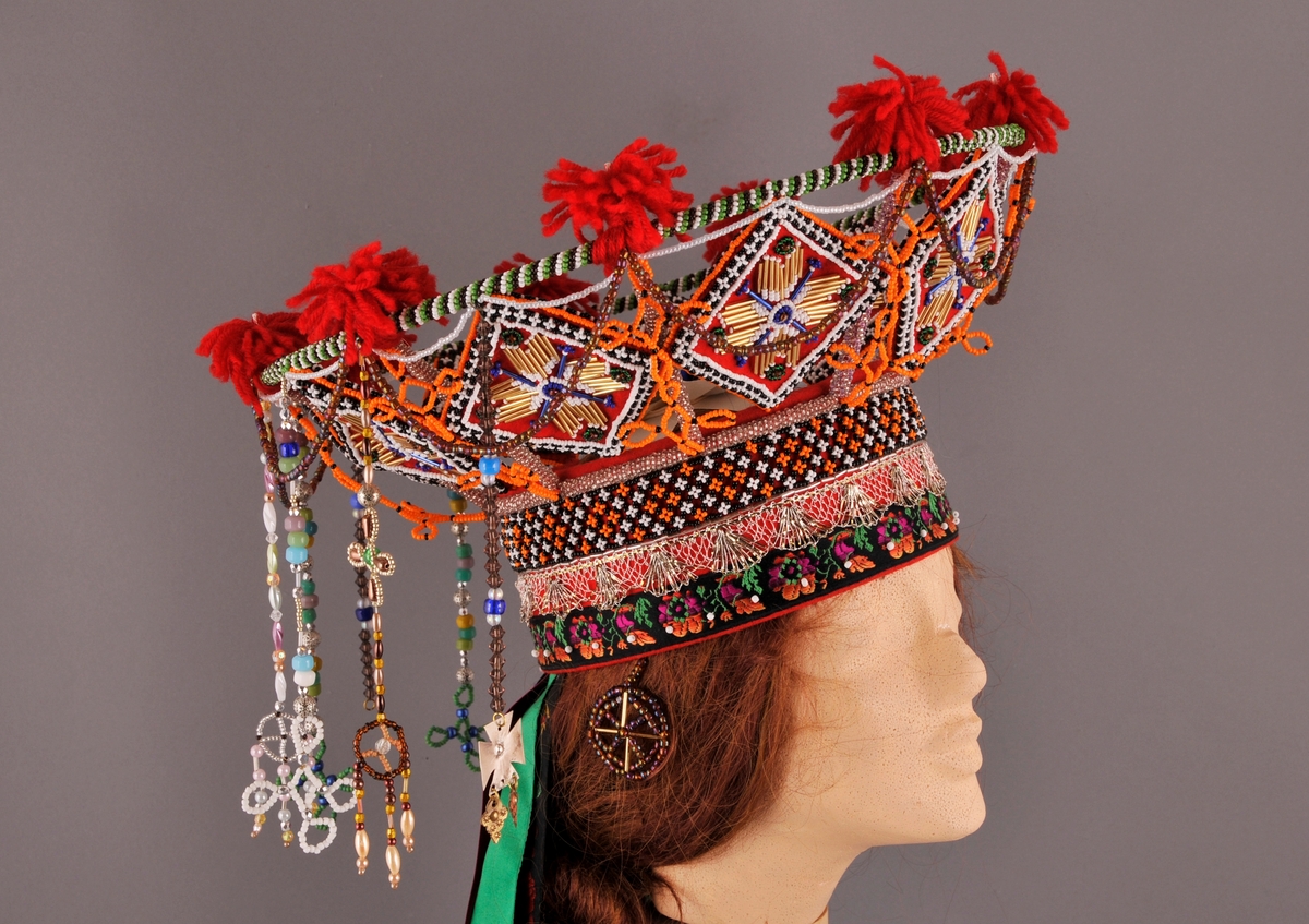 Brudekrone, nylaga.
"Pull" truleg med botn av stiv kartong og kledd med kraftig raudt klede. Påsydd (frå nedkant og oppover) eit band med satengbotn lansert blondemønster og påsydd kvite glasperler, ein sylvknipling og eit perlebendel. Perlebendelet er tredd med glasperler i svart, kvitt og orange.Sjølve krona er oppbygd rundt eit stativ av stål, raudlakkert. Heile stativet er dekt av glasperler i ulike fargar. Inni kvart "rom" er det eit sydd raudt kvadratisk klede som er pryda med glas- og stavperler av åttebladrose-mønster på begge sider, alle kvadrata er like og dei er montert på høgkant. I tillegg er det ein del ulike heng frå øvre kant av krona, her er det nytta ulike typer glasperler. På toppen av krona er det festa små duskar av laustvinna, raudt ullgarn i kvart skjæringspunkt. Inni krona, over hovudet, ligg eit ubleika band i kryss og i krysset er det sydd fast ein rosett.
Bak på krona er det sju heng av ulike band. På kvar side er det "øyrepynt". Frå sida og bakover er det 11 heng med ulike typer perler.