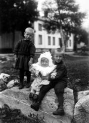 Tre barn stående oppstillt utenfor et våninghus. Foto enten 