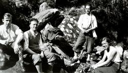 Foto av tre menn og en kvinne på fjelltur, og slapper her av