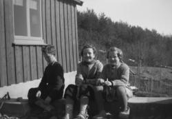 Foto av tre barn - en gutt og to piker - sittende utenfor et