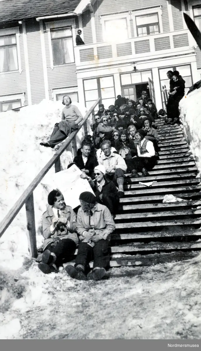 Foto av en stor gruppe mennesker som sitter i trappen
ved en turisthytte en vinterdag. Bildet er hentet fra fotoalbumet til Heide og kommer i serien med reg. nr. KMb-2008-022. Fra Nordmøre museums fotosamlinger. EFR2015
