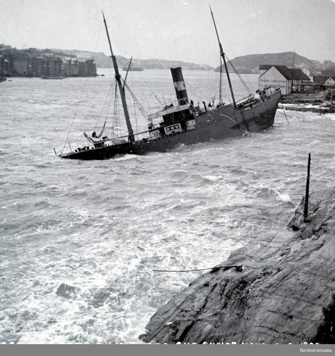 S/S Nordens stranding ved Chr Loennechens brygge i Sørsundet 12. februr 1903. Det var storm- og strømforhold som var årsaken til at den ikke fikk legge til kaien.  "Norden" som kom til Kristiansund med en saltlast, losset restpartiet på Hammervoldbrygga i Sørsundet. Ved avgangen var det stormbyger fra Nordvest så skipet greide ikke å avansere men drev ned mot sørspissen av Innlandet. Rutebåten "Nordmøre" forsøkte å assistere, men greide det ikke. "Norden" gikk på grunn med akterenden på Lervikskjæret på Innandet, og sank. Den ble provisorisk tettet og flyttet til Hønebukta, derifra til Trondheim og videre til Bergen. Dens senere skjebne er ukjendt. Fotograf er her trolig Ole Olsen Ranheimsæter. Fra Nordmøre museums fotosamlinger.