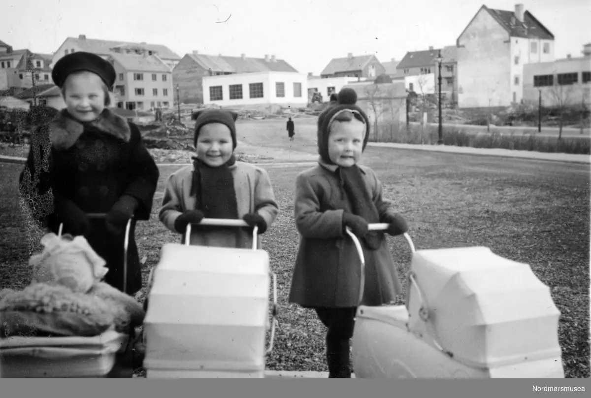 Foto av tre små barn med hver sin dukkevogn et sted i Kristiansund. Fra Nordmøre museums fotosamlinger. EFR2015