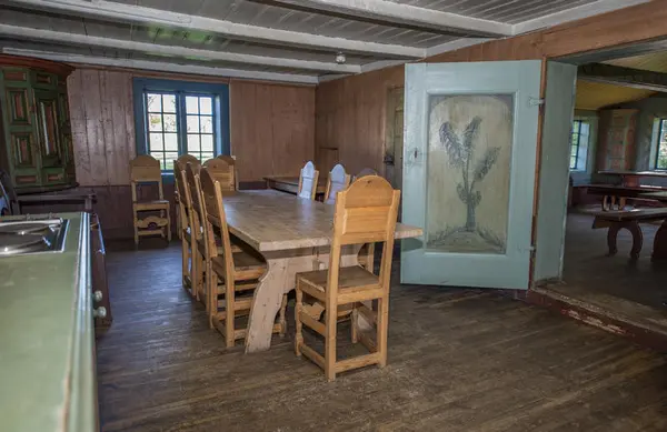 Barfrøstua har separat kjøkken med bred døra med dekormaleri av et tre. Møblering med langbord og trestoler med ryggstø samt en slagbenk.