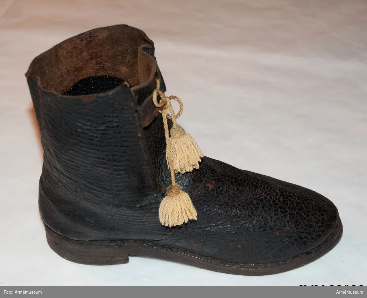 Känga av svart läder med snöre (senare tillägg). Det gula kängbandet på fotografier är AM.120193.