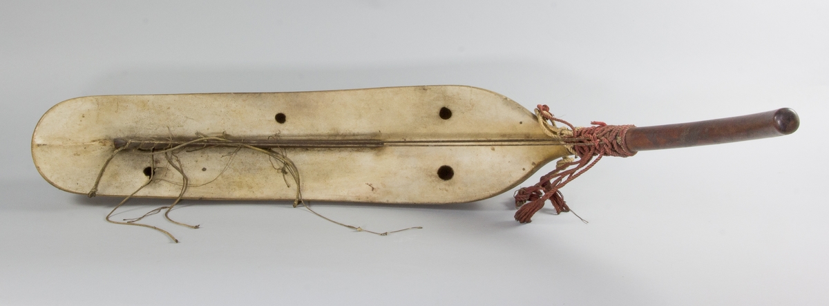 Harpa, båtformad av trä och överklädd med ljust skinn. Strängar, 4 st hela och ett flertal trasiga, av snöre. Halsen omlindad av grövre rött snöre. Under halsen trähandtag, spräckt.