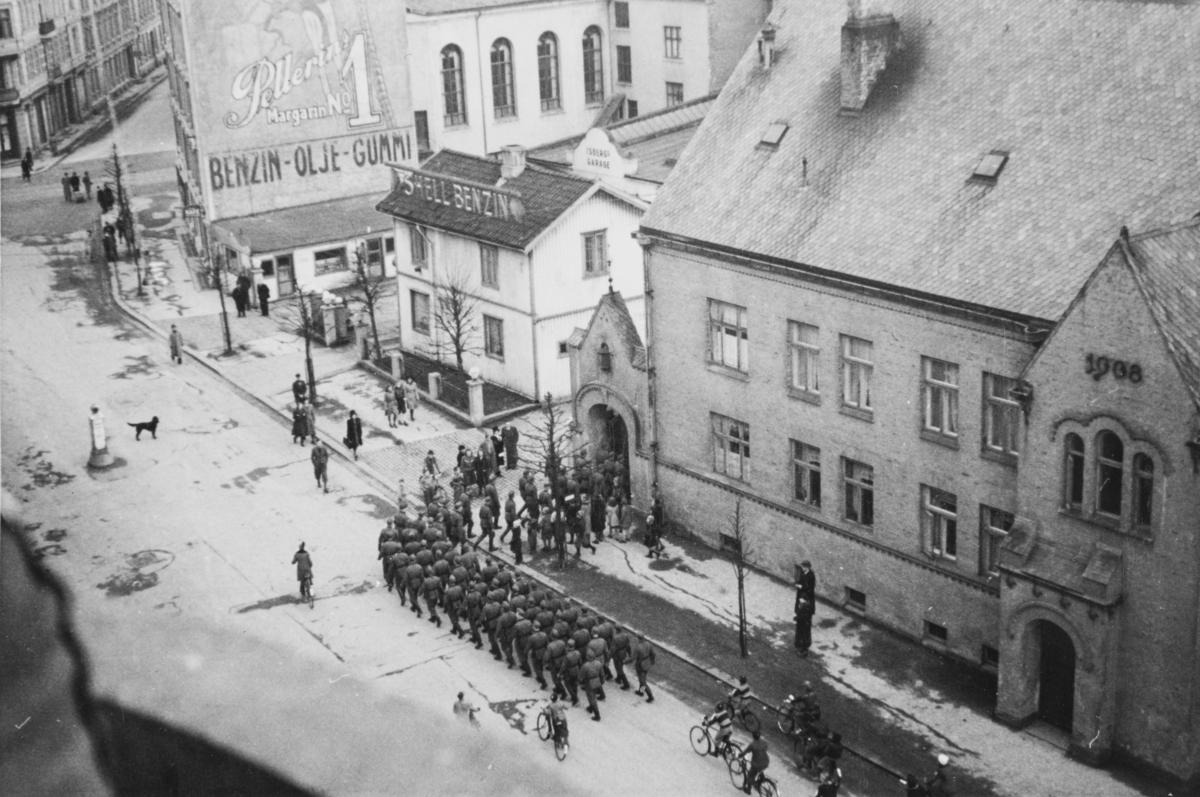Tyske tropper marsjerer fra Bogstadveien og inn på Majorstuen skole, som var tatt i bruk som kaserne. Tekst fra album: "- og under sang tilbake til skolen. April 1940."