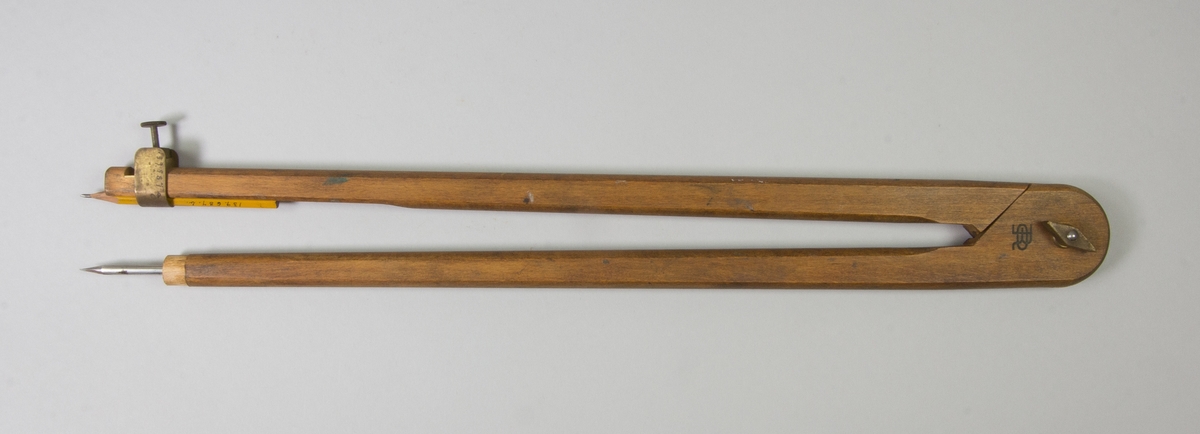Passare av trä med stift av järn och hållare av mässing för blyertspenna. Blyertspenna instucken i hållare på ena benet.