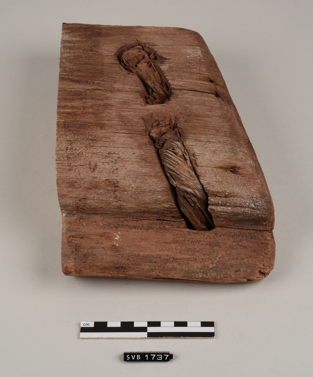 Del av bord til sydd båt. Det er hull med treplugger og sømhull med søm av røtter. Trematerialet har en rødlig farge. Antakelig på grunn av fargen på sanden der den var funnet.