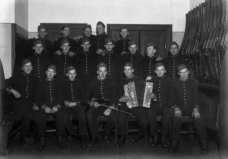 Foto av ett gäng "bassar", dvs meniga, i uniform. De är samlade i ett vapenrum på I 11, Växjö.