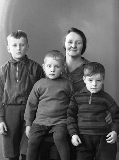 Foto av en mor med tre pojkar i vardagskläder.
Ateljéfoto.