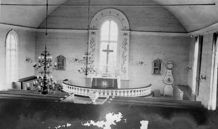 Interiör av Eringsboda kyrka sedd från läktaren. Över altargången hänger två ljuskronor. Utanför altarrundeln står dopfunten, och där innanför altarbordet med ljusstakar och ett kors. På väggen bakom hänger nummertavlorna. En klocka står till höger vid väggen.