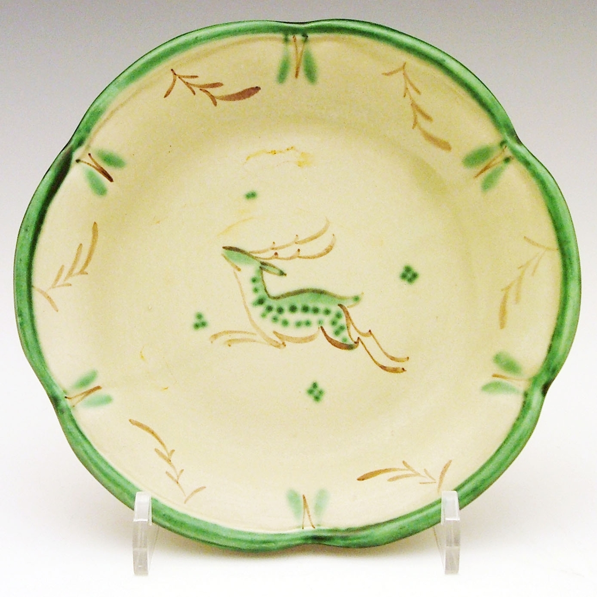Litet grönglaserat fat med grön och brun handmålad dekor i form av hjortdjur mot ljusare grön botten. Dekoren VA. Tillverkat vid Bo Fajans i Gävle mellan åren 1925-1943 och formgivet av Maggie Wibom.