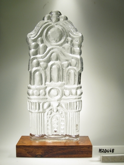 Glasskulptur.
Plattgjutet slott som monterats på en träplatta.
Klarglas.
"Blåsig" struktur.
Funktion: Glasskulptur