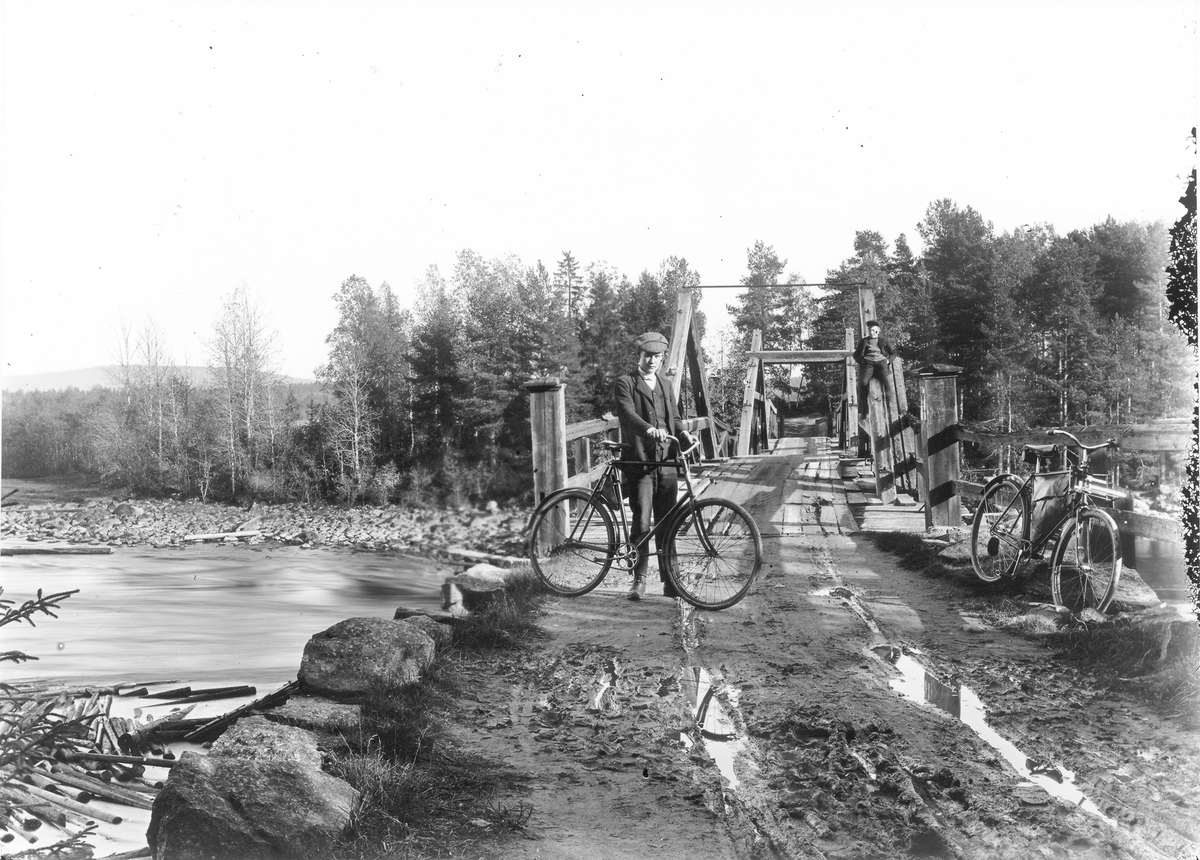 Bron över Ljusnan ungefär vid Exelan och över till Röstebo. Mannen med cykeln är Nils Dahlin, född 1893 och död 1968. Han bodde i Röstebo utanför Bollnäs. Mannen på broräcket är okänd. Cykeln som står till höger tillhörde fotografen Per Lindberg. Foto ca 1915.
Ny väg byggdes 1878-79 från Växbo mot Bollnäs i västlig riktning, över skogen till Röstebo och över Ljusnan och järnvägen fram till landsvägen Bollnäs-Arbrå. Vid Röstebo byggdes med hjälp från Ljusne älvs flottningsförening samt byarna Röstebo-Röste och Växbo bro över Ljusnan. Bron stod färdig våren 1879 och avprovades då synnerligen effektivt. Det var nämligen Ljusnan själv som utförde provet. Bron bestod inte provet, varför den delvis måste byggas om påföljande vinter. Underhållet av bron blev dock betungande, varför vägen omlades 1898 till sin nuvarande sträckning på östra sidan av Ljusnan ner till älvbron vid Rehn. Den forna byvägen är nu allmän väg och underhålles av vägdistriktet. Bron revs 1930.
