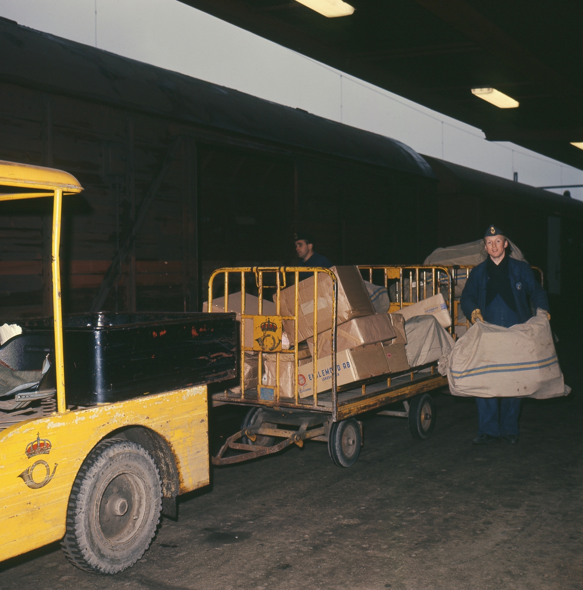 Lastning och lossning av post vid järnväg. Perrongtruck med släpvagn vid järnvägsvagn, 1960-talet.