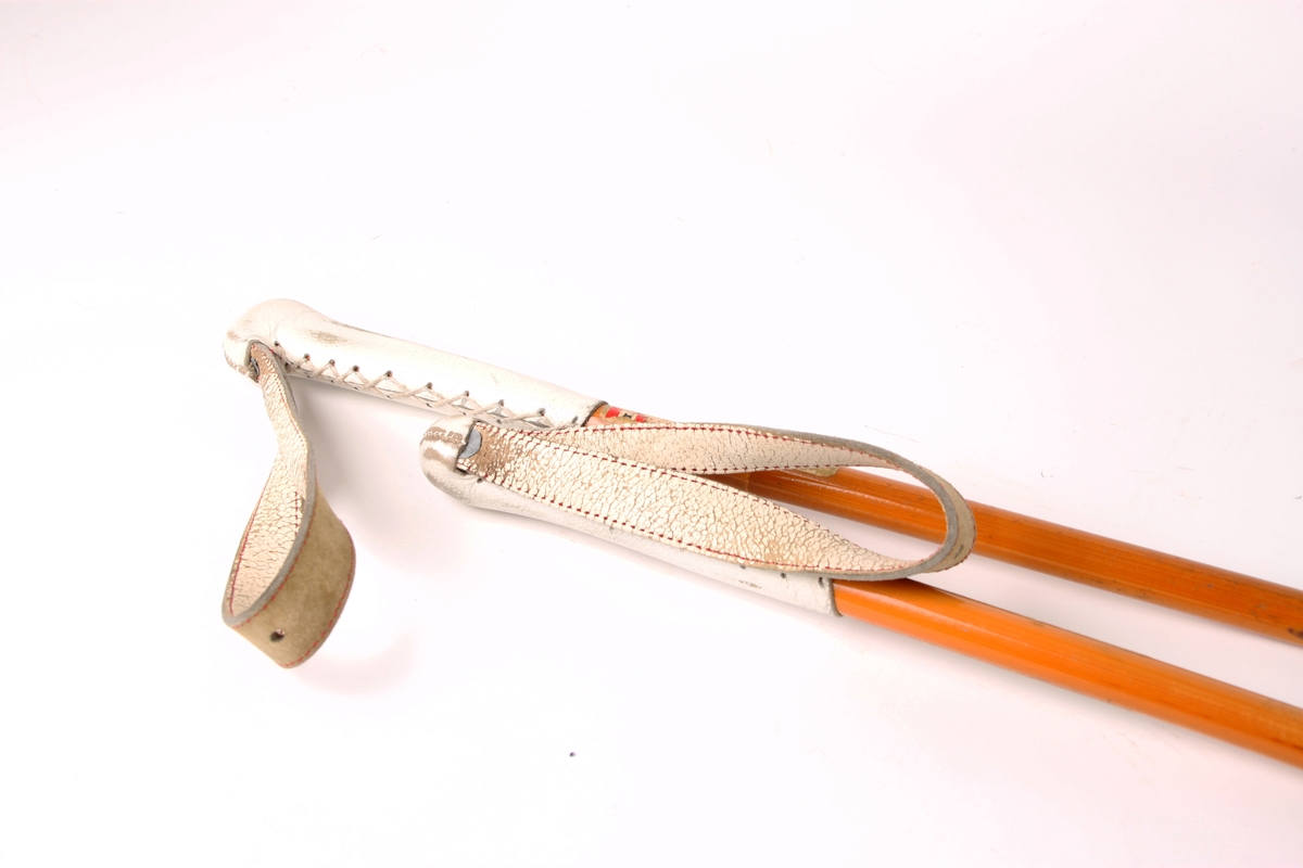 Et par bambusstaver med spanskrør/rotting-trinse med røde lærkryss. Stavene har påsydde lærhåndtak og sydde håndstropper i hvit farge.
