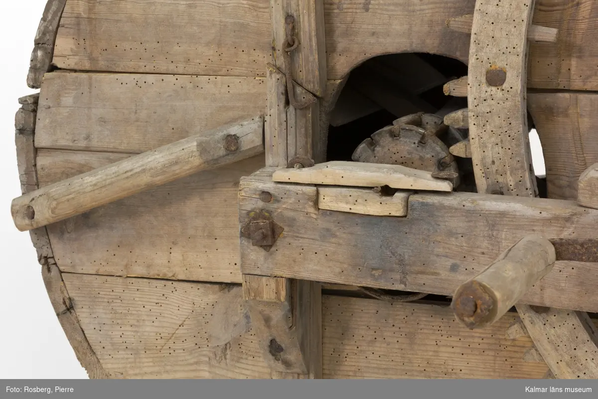 KLM 6738. Kastverk. Dialektalt kallad för kastvanna eller kastmaskin. Av trä och järn. Åkerbruksredskap av gammal form som har använts för rensning av säd. Kastverket är främst tillverkad av trä, som maskinens axel, dess två handtag samt taggade hjul med fyra ekrar. Vev och andra mindre delar av maskinen är av järn. Kastverket går att öppna genom att lossa två haspar som sitter på vardera långsida av maskinen.