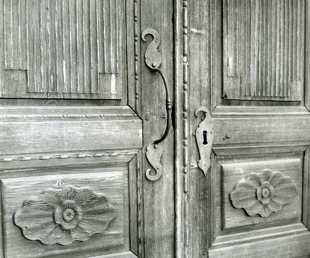 Detalj av en pardörr med snidade dörrspeglar och metallhandtag.