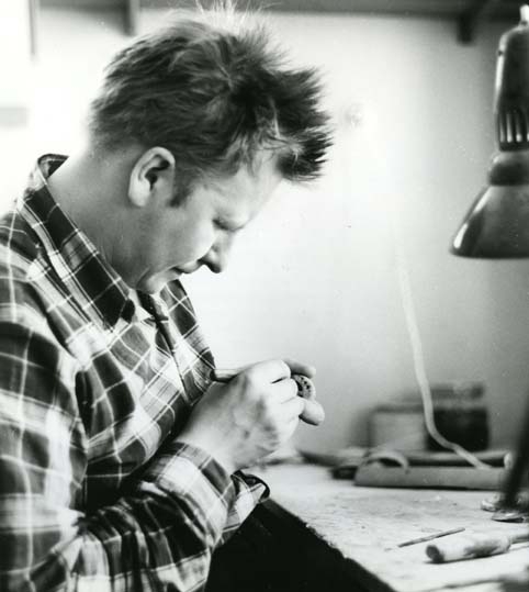 Konstnären Lars Pirak sitter vid sitt arbetsbord och karvar in samiska tecken i ett föremål.