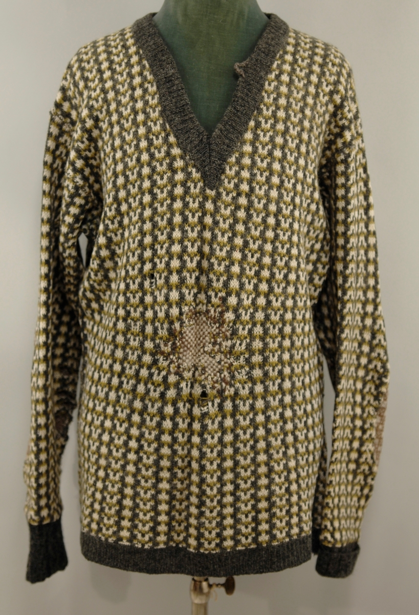 Ullgenser med v-utringning, grå/hvit med gult mønster. Innfelt stykke på albuen fra en annen genser, brunt og hvitt. 