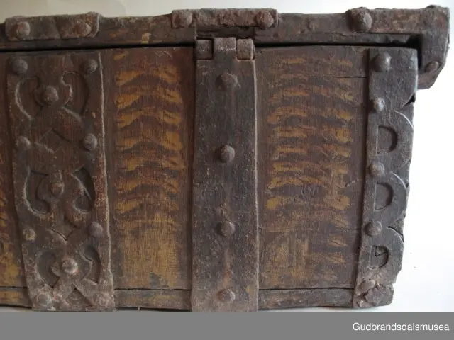 "Rik gjenombroten jarning over heile skrinet. Gamal type, alder uviss. Fra Vestre Gausdal". (Jf. "Katalog for Lom Bygdesamling,1925"). 
Skrinet har 3 rom, nøkkelhullslås og jernhandtak på sidene. Lokket er satt sammen av 2 bord, er festet til utsiden på bakstykket med to hengselbeslag og har 2 sidelister festet med trenagler. Bunnen er satt sammen av 2 bord, festet til hverandre med 2 forsenka trenagler; bunnen er festet til skrinrammen med trenagler.  Skrinrammen er tappet og forsterket med hjørnekantbeslag utvendig. 
Skrinet har jernbeslag med gjennombrutt mønster, 5 stk. B: 6,5 x L: 45 cm på lokk, 3 på hhv. bakstykke, front og sidestykker B: 6,5 x 20 cm. Lokket har ett låsbeslag og de to øvre hengselbeslag festet på innsiden, de to nedre hengselbeslag er festet på utsiden av bakstykket. Alle beslag er festet med store jernnagler samt festet under bunn på skrinet. De to hengselbeslag har også gjennombrutt mønster.  Nøkkelhullslåsen mangler låsanordning på innsiden.
DEKOR. Malingen har blitt beskyttet med et lag ferniss el.l., noe som ble vanlig fra begynnelsen av 1700-tallet. Ingen skurddekor. I stedet er beslag av jern brukt som dekorelement, noe som periodemessig kan peke på 1600-tallet, tidlig 1700-tallet, der treskurden ikke var fremherskende. Liknende dekorbruk finner du på LBY0328. Skrinet har gjennombrutt mønster på beslag og store jernnagler som beslagfeste. Treverket som synes mellom beslagene er malt med horisontale bølgestrukturer i gul og brun. Den dominerende dekorfargen er brun og gul, men det finnes små rester av blå eller blågrønn på lokk, sidelister på lokk, front og bunnkant på bakstykket samt av gul på frontbeslag. Innsiden av lokket er malt i terracottarød nyanse. Tradisjonelt fremkom denne fargen ved bruk av saft fra orr blandet med spytt, som ble smurt ut over treet. 
BRUK. Før kofferten kom i bruk hadde man reiseskrinet, som ble brukt til oppbevaring av bl.a. klær, verdisaker og mat på reiser. Skrinet hadde ofte et eller to mindre, smale rom langs den ene skrinsiden og ett større rom. De fleste reiseskrin var i tillegg forsterket med jernbeslag langs alle kanter og med en solid nøkkelhullås til sikring mot støt, slag og tyveri.