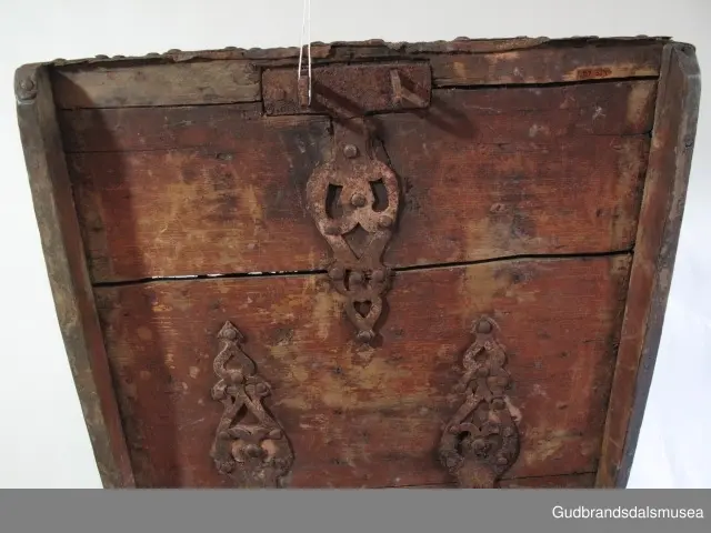 "Rik gjenombroten jarning over heile skrinet. Gamal type, alder uviss. Fra Vestre Gausdal". (Jf. "Katalog for Lom Bygdesamling,1925"). 
Skrinet har 3 rom, nøkkelhullslås og jernhandtak på sidene. Lokket er satt sammen av 2 bord, er festet til utsiden på bakstykket med to hengselbeslag og har 2 sidelister festet med trenagler. Bunnen er satt sammen av 2 bord, festet til hverandre med 2 forsenka trenagler; bunnen er festet til skrinrammen med trenagler.  Skrinrammen er tappet og forsterket med hjørnekantbeslag utvendig. 
Skrinet har jernbeslag med gjennombrutt mønster, 5 stk. B: 6,5 x L: 45 cm på lokk, 3 på hhv. bakstykke, front og sidestykker B: 6,5 x 20 cm. Lokket har ett låsbeslag og de to øvre hengselbeslag festet på innsiden, de to nedre hengselbeslag er festet på utsiden av bakstykket. Alle beslag er festet med store jernnagler samt festet under bunn på skrinet. De to hengselbeslag har også gjennombrutt mønster.  Nøkkelhullslåsen mangler låsanordning på innsiden.
DEKOR. Malingen har blitt beskyttet med et lag ferniss el.l., noe som ble vanlig fra begynnelsen av 1700-tallet. Ingen skurddekor. I stedet er beslag av jern brukt som dekorelement, noe som periodemessig kan peke på 1600-tallet, tidlig 1700-tallet, der treskurden ikke var fremherskende. Liknende dekorbruk finner du på LBY0328. Skrinet har gjennombrutt mønster på beslag og store jernnagler som beslagfeste. Treverket som synes mellom beslagene er malt med horisontale bølgestrukturer i gul og brun. Den dominerende dekorfargen er brun og gul, men det finnes små rester av blå eller blågrønn på lokk, sidelister på lokk, front og bunnkant på bakstykket samt av gul på frontbeslag. Innsiden av lokket er malt i terracottarød nyanse. Tradisjonelt fremkom denne fargen ved bruk av saft fra orr blandet med spytt, som ble smurt ut over treet. 
BRUK. Før kofferten kom i bruk hadde man reiseskrinet, som ble brukt til oppbevaring av bl.a. klær, verdisaker og mat på reiser. Skrinet hadde ofte et eller to mindre, smale rom langs den ene skrinsiden og ett større rom. De fleste reiseskrin var i tillegg forsterket med jernbeslag langs alle kanter og med en solid nøkkelhullås til sikring mot støt, slag og tyveri.