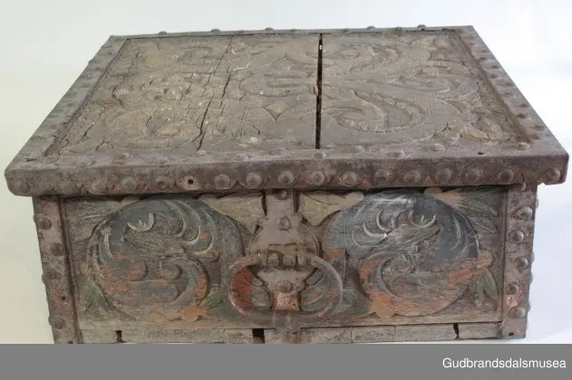 "Bladformer, smøygde band og drageornamentikk. Millom kantjarn og utskurden hev lokket fint utskorne små blad og halvrunde aggar. Vel vedlikehalde, sterk jarning og prydelege gangjarn. Truleg frå 1500 talet. Fra Haugen, Øystre Gausdal". (Jf. "Katalog for Lom Bygdesamling,1925).
Skrinrammen er holdt sammen av utvendige hjørnekantbeslag; jernhandtak i hver side. Fronten har nøkkelhullslås med beslag rundt. Lokket er satt samen av 2 bord, forsterket med jernbeslag rundt kanter på overside; to hengselbeslag festet til innside av lokk og bakstykke. Skrinsider blir holdt sammen av beslag ned langs hjørnekanter; har jernhandtak festet på jernbeslag.
Bunnen er satt sammen av 2 bord, festet til hverandre med to forsenka treplugger; bunnen var opprinnelig festet til underkant av skrinsider med 4 x 4 trenagler,seinere festet med spiker. 
Det er jernbeslag  på bakstykket midt, rundt hjørnekanter, omkring nøkkelhullslås, rundt lokk samt 2 handtak med beslag. Alle beslag er festet med store jernnagler; beslag på sidestykker er festet med små jernnagler under skrinbunnen. 3 av 8 bunnfester for beslag er fortsatt intakte.
DEKOR. De store jernnaglene med forskjøvet plassering på beslag ble sannsynligvis brukt som dekorelement; runde beslag på sider, bakstykke og front. Flatskurd på lokk med flettet, stilisert renessanseranke, der bladverk er "omgjort" til småspiraler eller rundinger.  På skrinsidene akantusskurd med c-former, bladtunger uten stilk og naturalistiske småblad i rokokkostil. Flatskurd var vanlig i Gudbrandsdalen i perioden ca. 1650-1750, mens akantusmotivet først ble vanlig på bruksgjenstander i løpet av siste halvdel av 1700-tallet. Den mørkere grønne og blå dekorfargen var vanlig i siste del på 1700-tallet; den brune bunnfargen var vanlig i bruk fra 1780-tallet. 
BRUK. Før kofferten kom i bruk hadde man reiseskrinet, som ble brukt til oppbevaring av bl.a. klær, verdisaker og mat på reiser. Skrinet hadde ofte et eller to mindre, smale rom langs den ene skrinsiden og ett større rom. De fleste reiseskrin var i tillegg forsterket med jernbeslag langs alle kanter og med en solid nøkkelhullås til sikring mot støt, slag og tyveri.