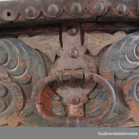 "Bladformer, smøygde band og drageornamentikk. Millom kantjarn og utskurden hev lokket fint utskorne små blad og halvrunde aggar. Vel vedlikehalde, sterk jarning og prydelege gangjarn. Truleg frå 1500 talet. Fra Haugen, Øystre Gausdal". (Jf. "Katalog for Lom Bygdesamling,1925).
Skrinrammen er holdt sammen av utvendige hjørnekantbeslag; jernhandtak i hver side. Fronten har nøkkelhullslås med beslag rundt. Lokket er satt samen av 2 bord, forsterket med jernbeslag rundt kanter på overside; to hengselbeslag festet til innside av lokk og bakstykke. Skrinsider blir holdt sammen av beslag ned langs hjørnekanter; har jernhandtak festet på jernbeslag.
Bunnen er satt sammen av 2 bord, festet til hverandre med to forsenka treplugger; bunnen var opprinnelig festet til underkant av skrinsider med 4 x 4 trenagler,seinere festet med spiker. 
Det er jernbeslag  på bakstykket midt, rundt hjørnekanter, omkring nøkkelhullslås, rundt lokk samt 2 handtak med beslag. Alle beslag er festet med store jernnagler; beslag på sidestykker er festet med små jernnagler under skrinbunnen. 3 av 8 bunnfester for beslag er fortsatt intakte.
DEKOR. De store jernnaglene med forskjøvet plassering på beslag ble sannsynligvis brukt som dekorelement; runde beslag på sider, bakstykke og front. Flatskurd på lokk med flettet, stilisert renessanseranke, der bladverk er "omgjort" til småspiraler eller rundinger.  På skrinsidene akantusskurd med c-former, bladtunger uten stilk og naturalistiske småblad i rokokkostil. Flatskurd var vanlig i Gudbrandsdalen i perioden ca. 1650-1750, mens akantusmotivet først ble vanlig på bruksgjenstander i løpet av siste halvdel av 1700-tallet. Den mørkere grønne og blå dekorfargen var vanlig i siste del på 1700-tallet; den brune bunnfargen var vanlig i bruk fra 1780-tallet. 
BRUK. Før kofferten kom i bruk hadde man reiseskrinet, som ble brukt til oppbevaring av bl.a. klær, verdisaker og mat på reiser. Skrinet hadde ofte et eller to mindre, smale rom langs den ene skrinsiden og ett større rom. De fleste reiseskrin var i tillegg forsterket med jernbeslag langs alle kanter og med en solid nøkkelhullås til sikring mot støt, slag og tyveri.